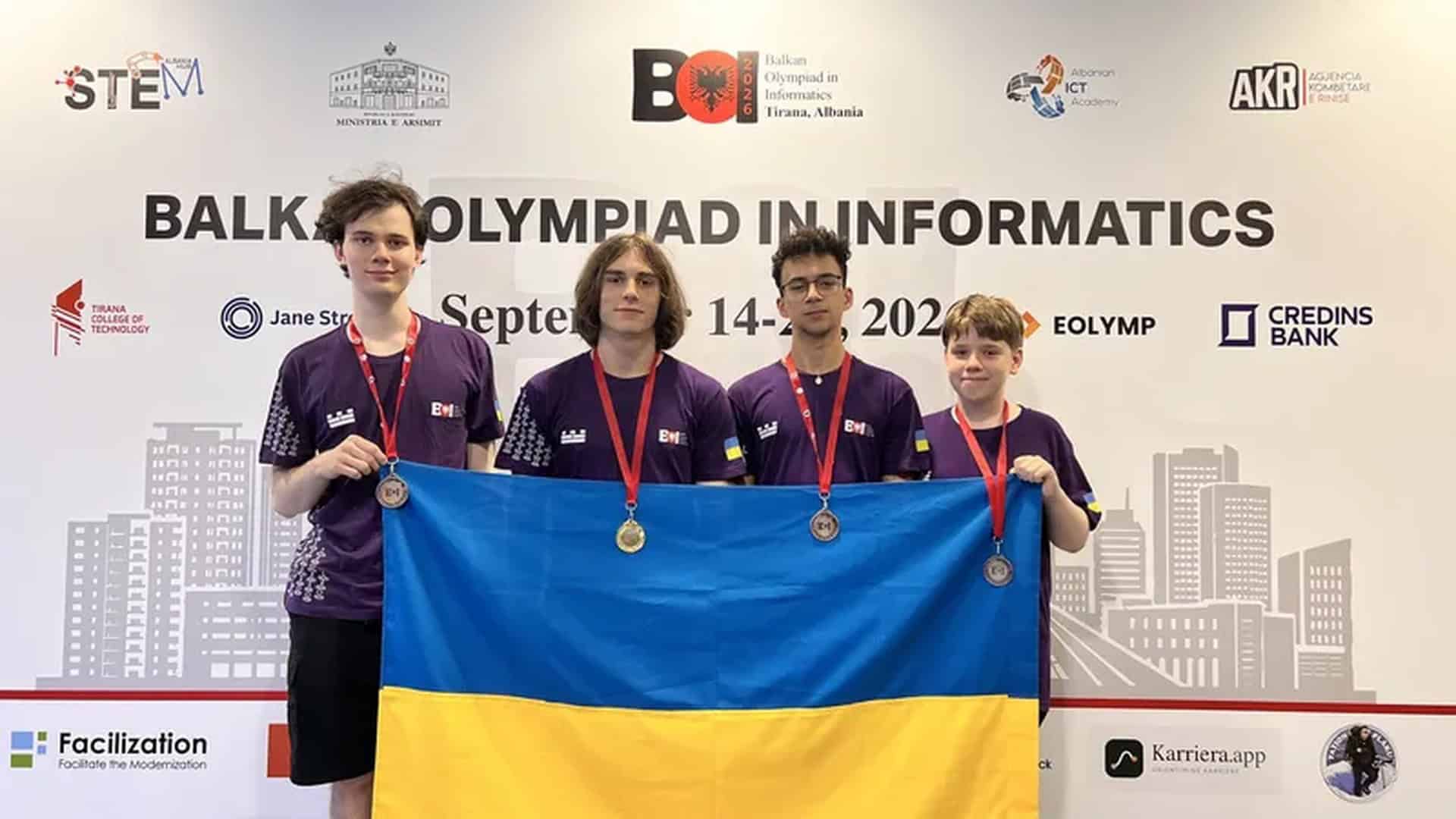 Чотири українські школярі з медалями тримають прапор України на фоні банера Балканської олімпіади з інформатики в Тирані