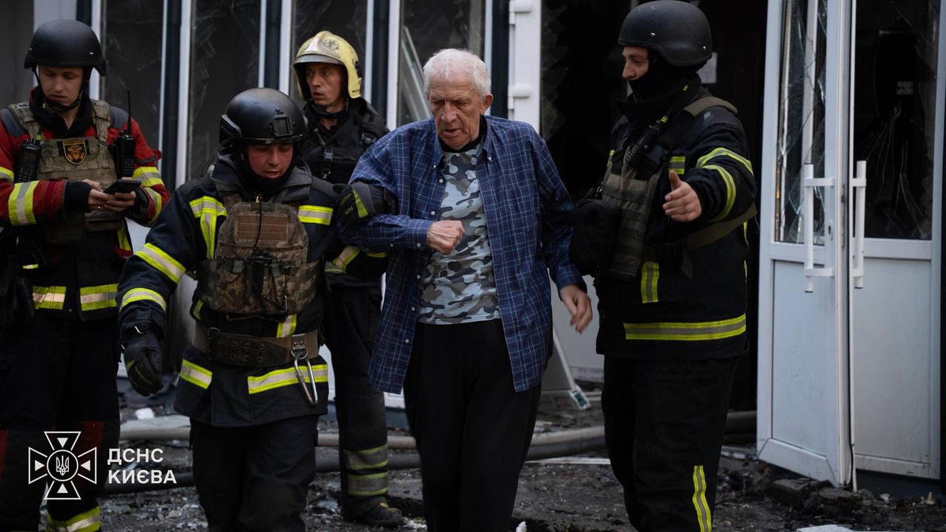 Уламки дронів впали на ЖК у Голосіївському та на подвір’я у Святошинському Рятувальники ДСНС виводять літнього чоловіка з пошкодженої будівлі повз розбиті скляні двері після пожежі