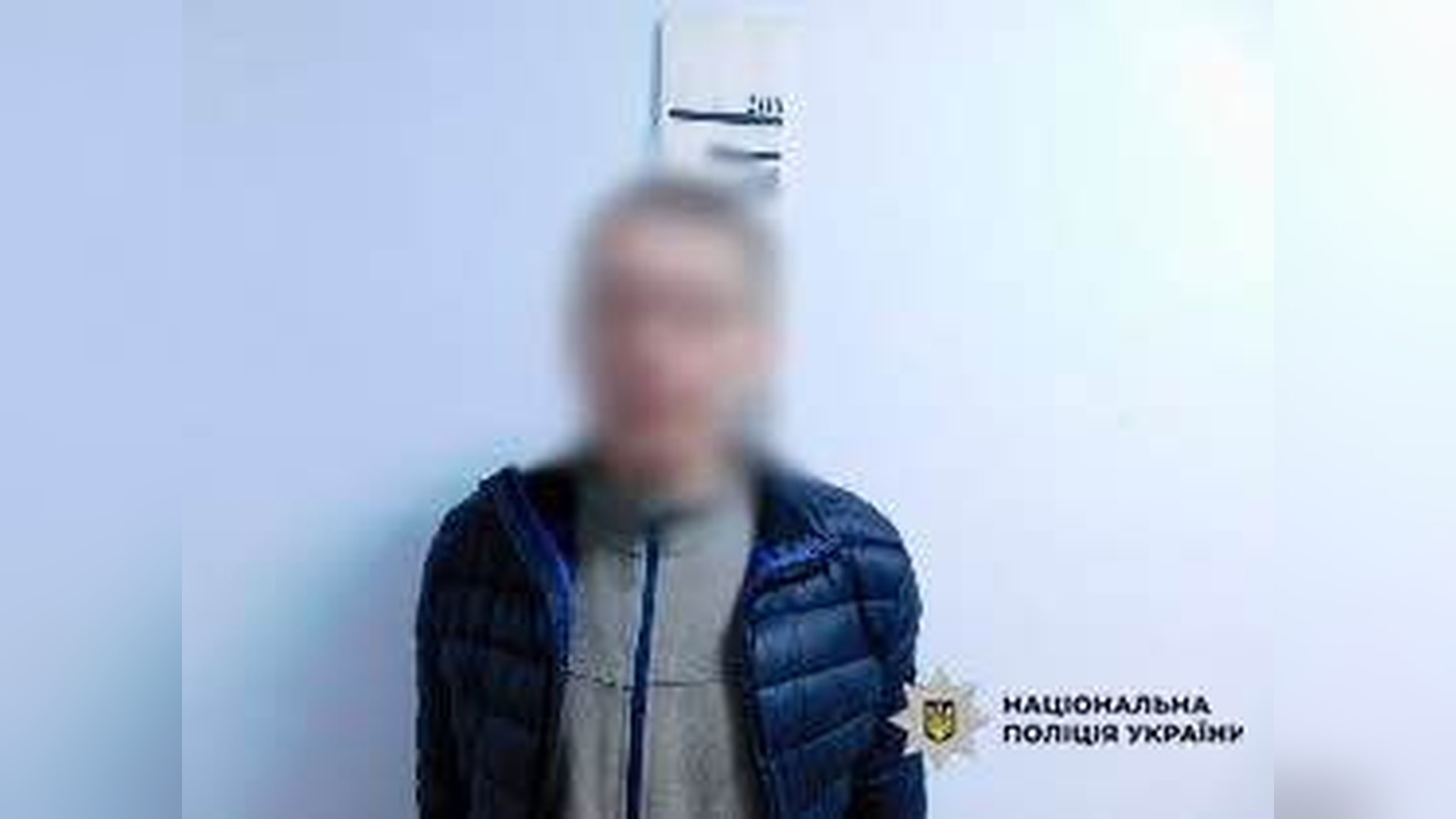 Затриманий 38-річний киянин у синій куртці з розмитим обличчям на тлі стіни, у кутку — логотип Національної поліції України