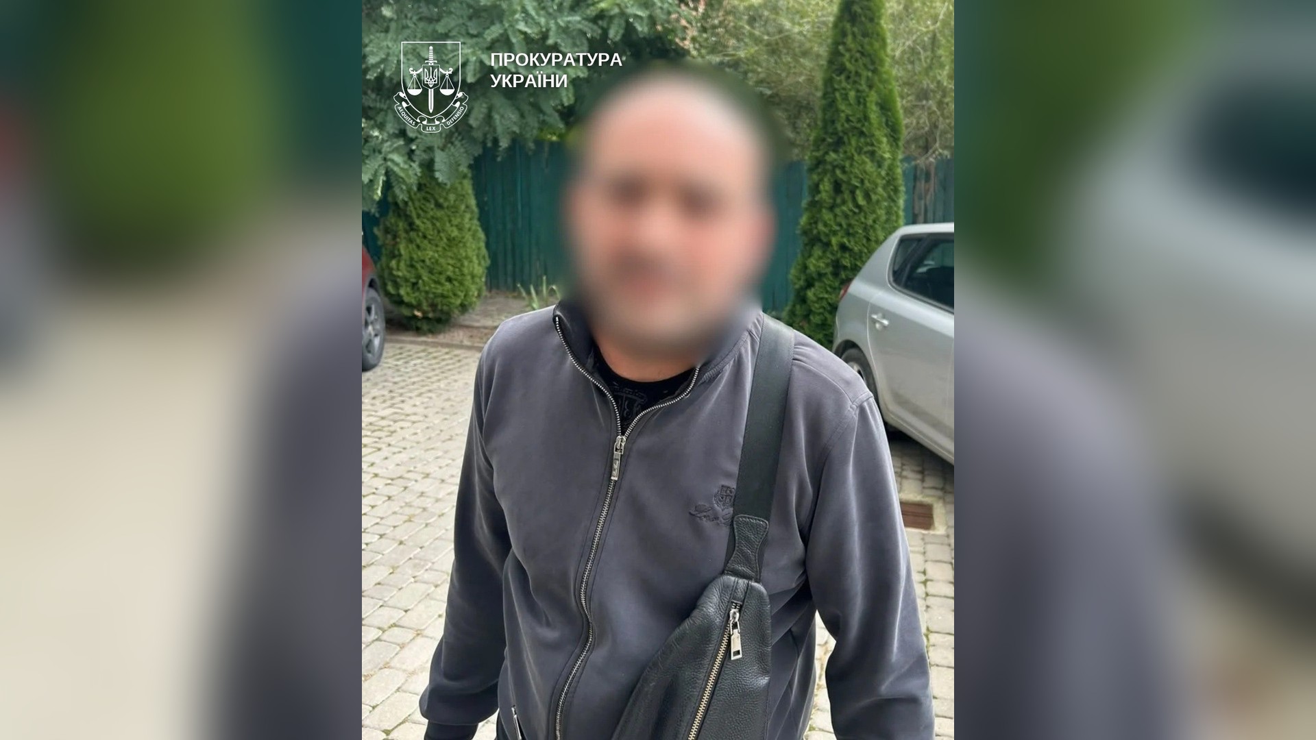 Киянина підозрюють у крадіжці телефона в переході під час ракетної атаки Чоловік у сірій кофті з розмитим обличчям і сумкою через плече на подвір’ї біля автомобіля, у кутку — логотип Прокуратури України