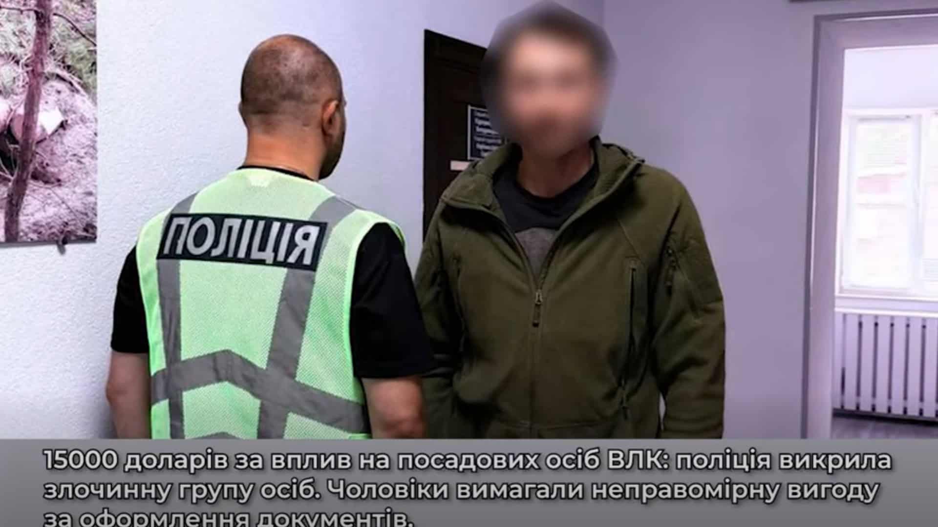 Поліцейський стоїть поруч із затриманим чоловіком у приміщенні відділку під час розслідування справи про вимагання 15 000 доларів за вплив на ВЛК