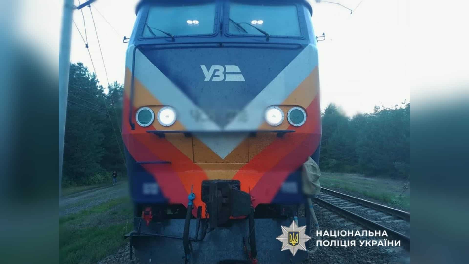 Передня частина локомотива «Укрзалізниці» на залізничній колії, поруч ліс і опора контактної мережі