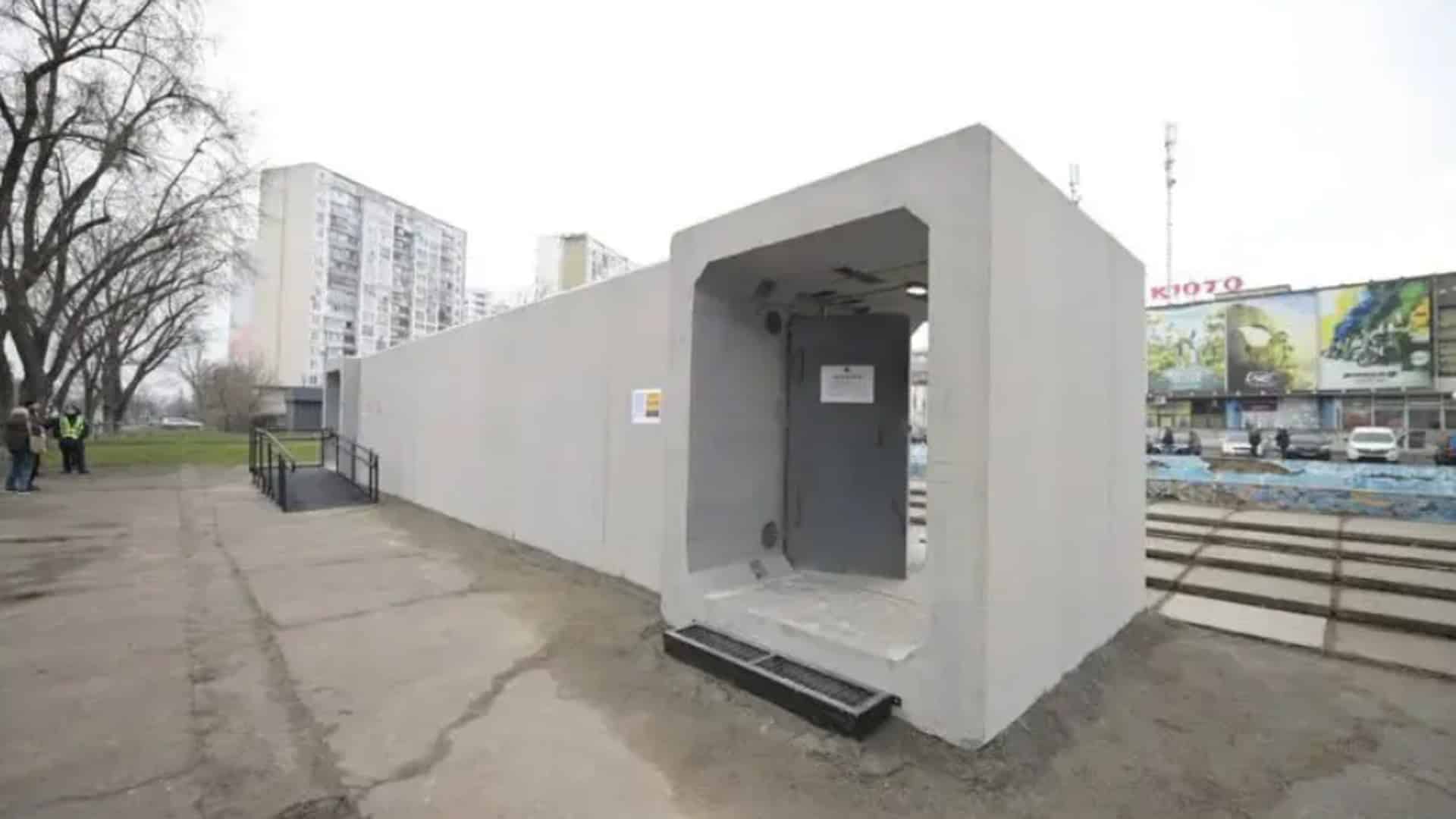 Ремонт огорожі Байкового кладовища: 46 млн без конкурсу Бетонне мобільне укриття з металевими дверима встановлене біля зупинки громадського транспорту в Києві на фоні багатоповерхівок.
