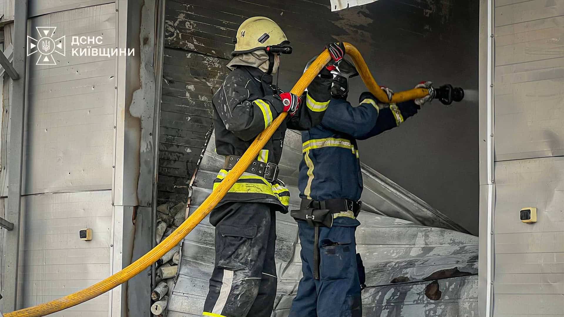 Двоє рятувальників ДСНС у задимленому приміщенні тримають пожежний рукав і спрямовують струмінь води на осередок займання
