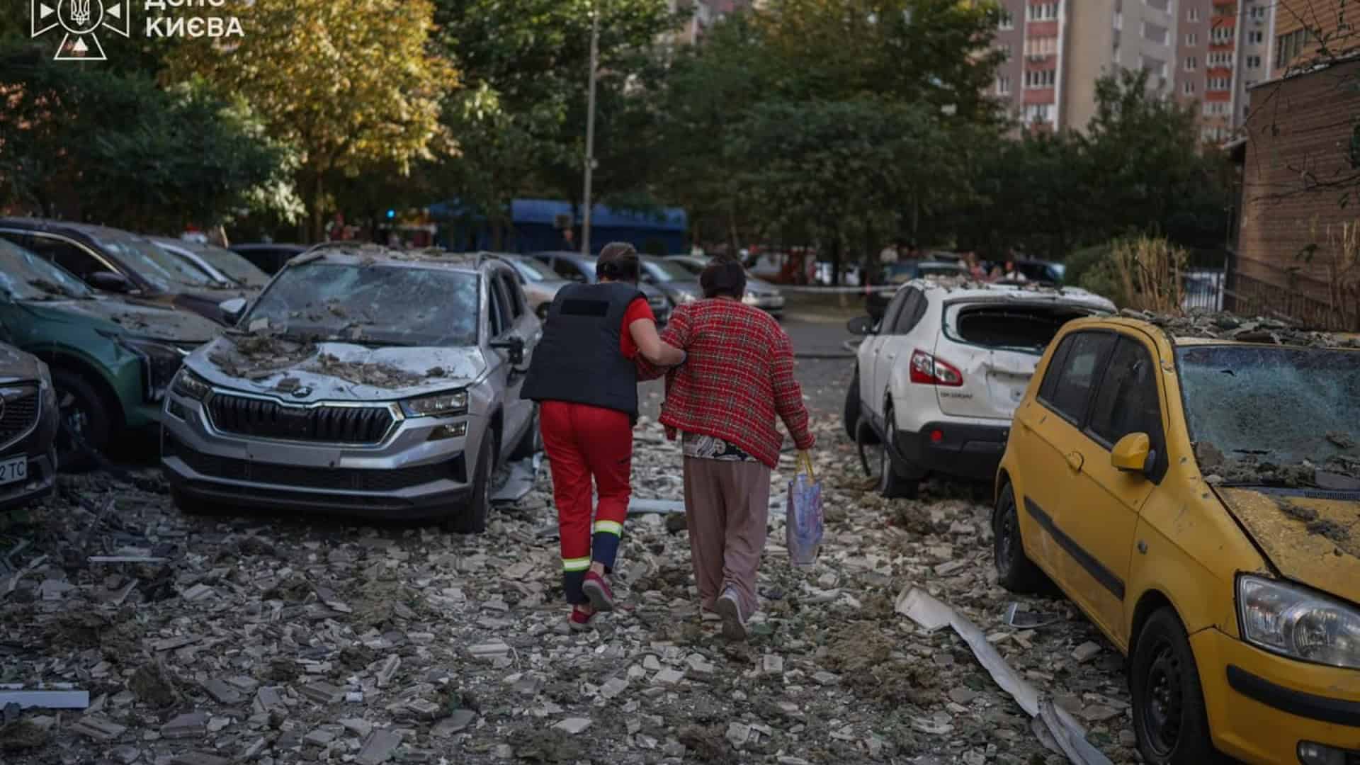 Жінки йдуть через уламки та скло повз пошкоджені автомобілі у дворі житлового кварталу після удару по Києву