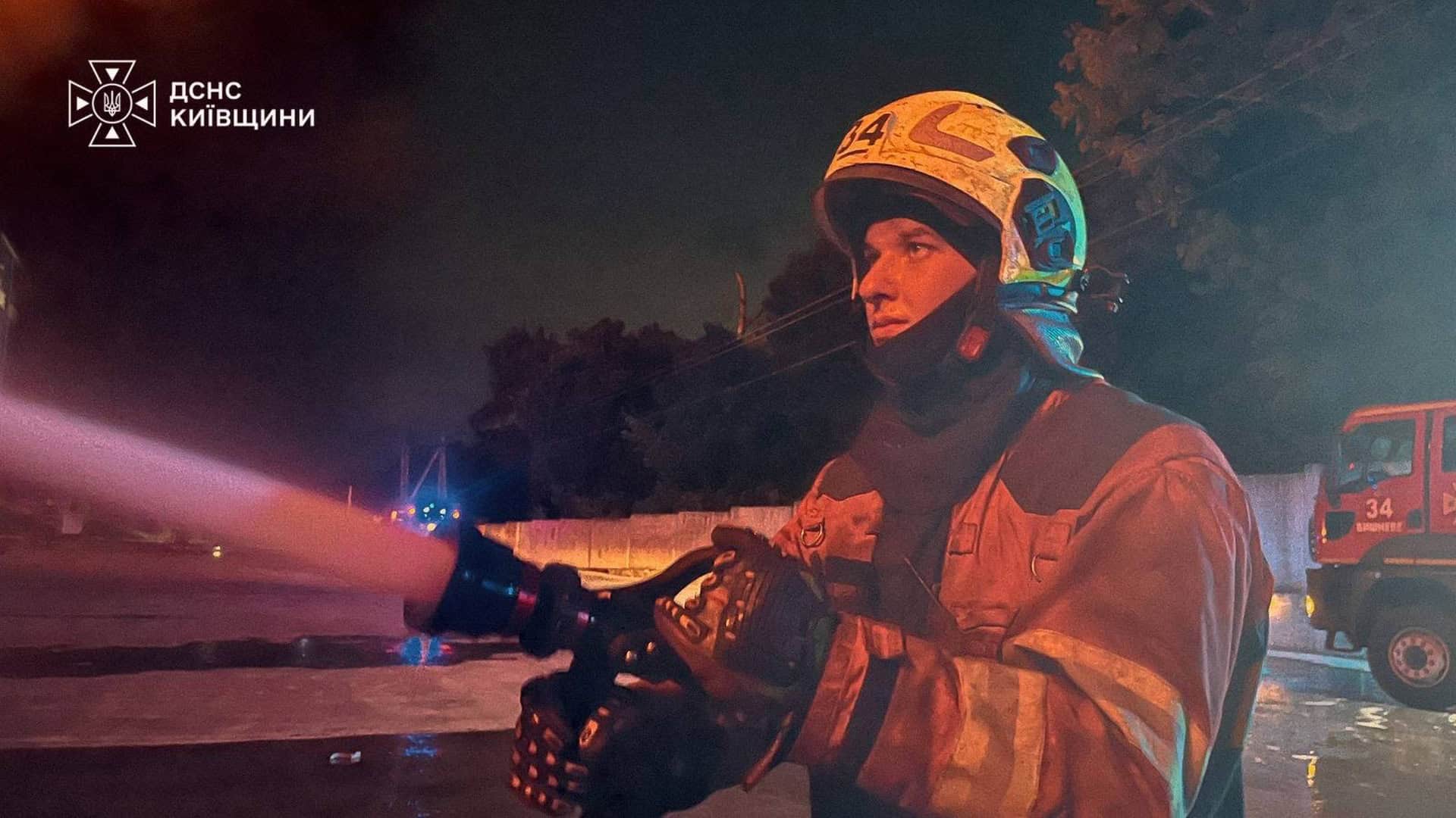Рятувальник ДСНС Київщини з пожежним рукавом вночі на місці пожежі в Бучанському районі після удару 11 вересня