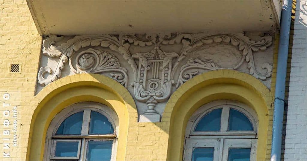 Ліпний декор із лірою та завитками між двома арковими вікнами під балконом будинку на Великій Васильківській, 26 у Києві