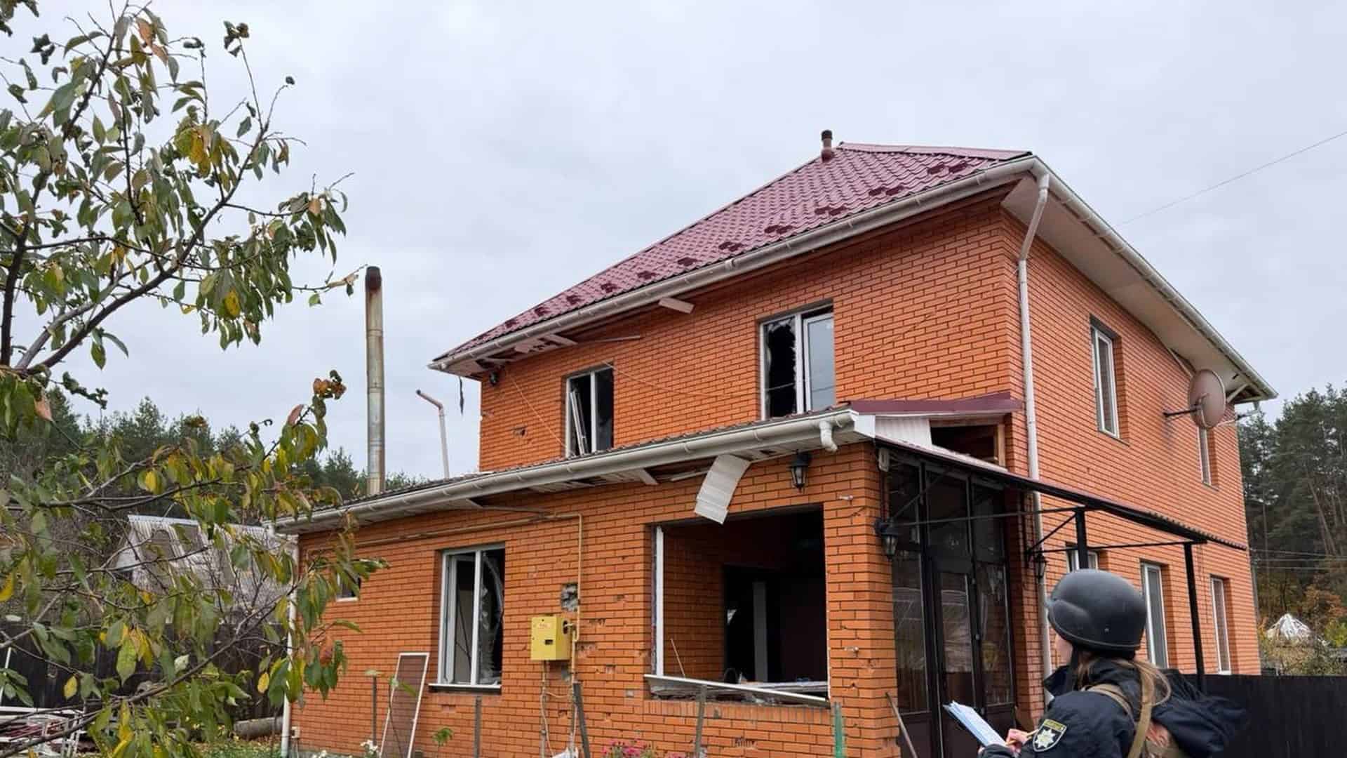 Поліцейська оглядає пошкоджений після російської атаки цегляний приватний будинок із вибитими вікнами на Київщині