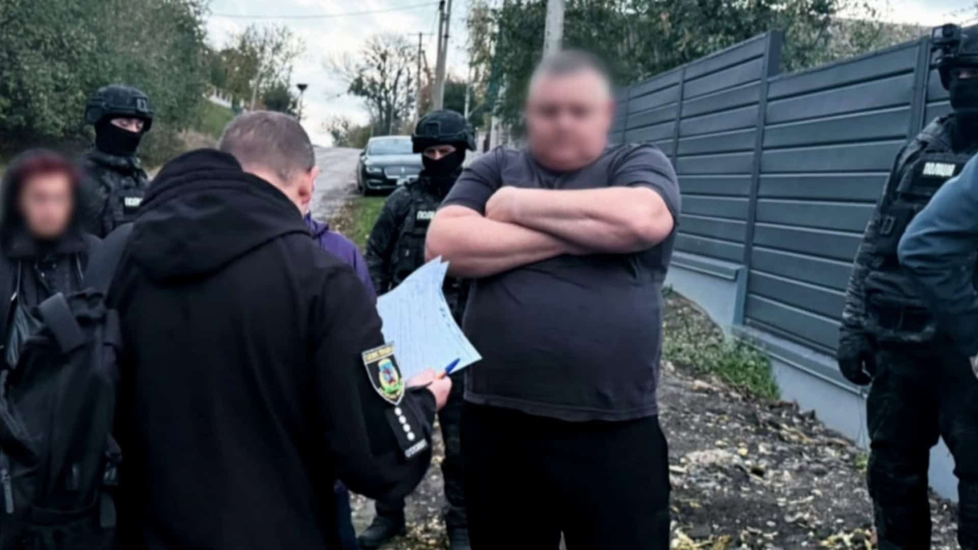 Поліцейські та спецпризначенці біля паркану під час вручення підозри чоловікові із заблюреним обличчям на Білоцерківщині