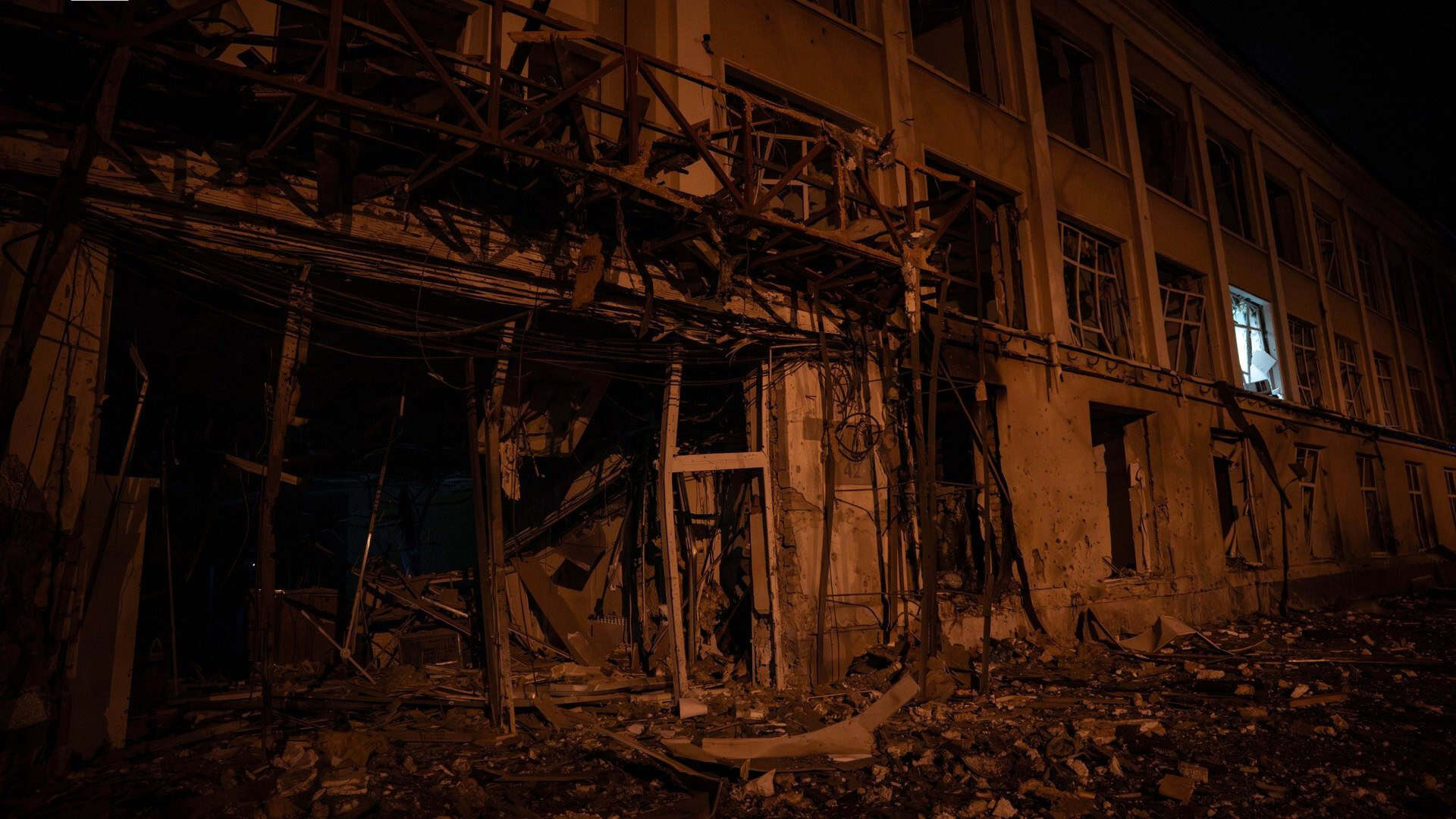 Частково зруйнований фасад триповерхової будівлі вночі після балістичної атаки на Київ, уламки на тротуарі
