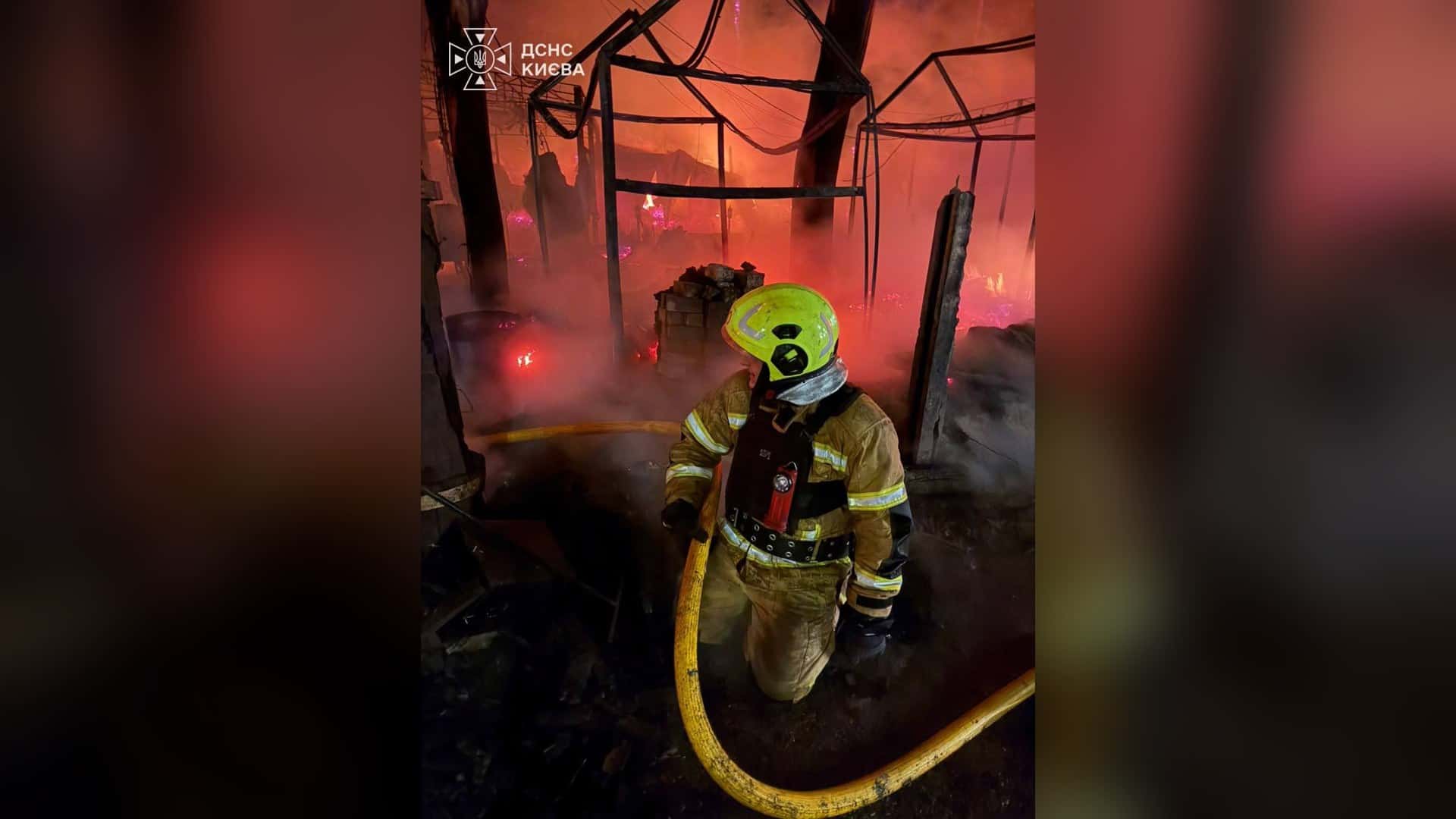 Рятувальник ДСНС Києва з рукавом гасить пожежу серед обгорілих конструкцій після балістичної атаки на Київ 22 жовтня