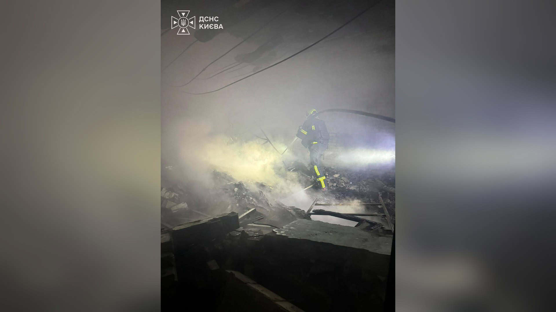 Рятувальник ДСНС Києва гасить пожежу серед уламків у задимленому приміщенні після атаки на столицю