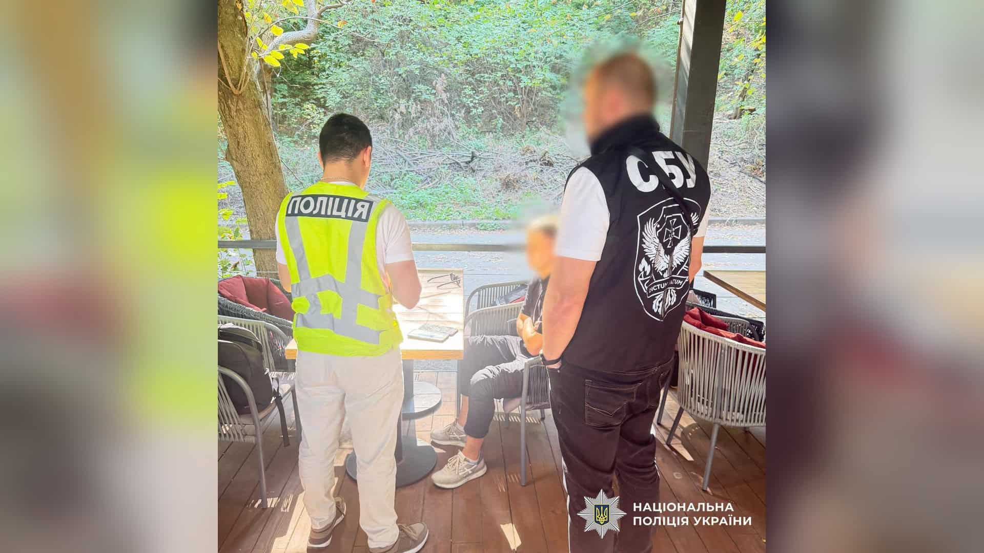 Поліцейський і співробітник СБУ біля затриманого чоловіка за столиком літнього майданчика кафе в Києві
