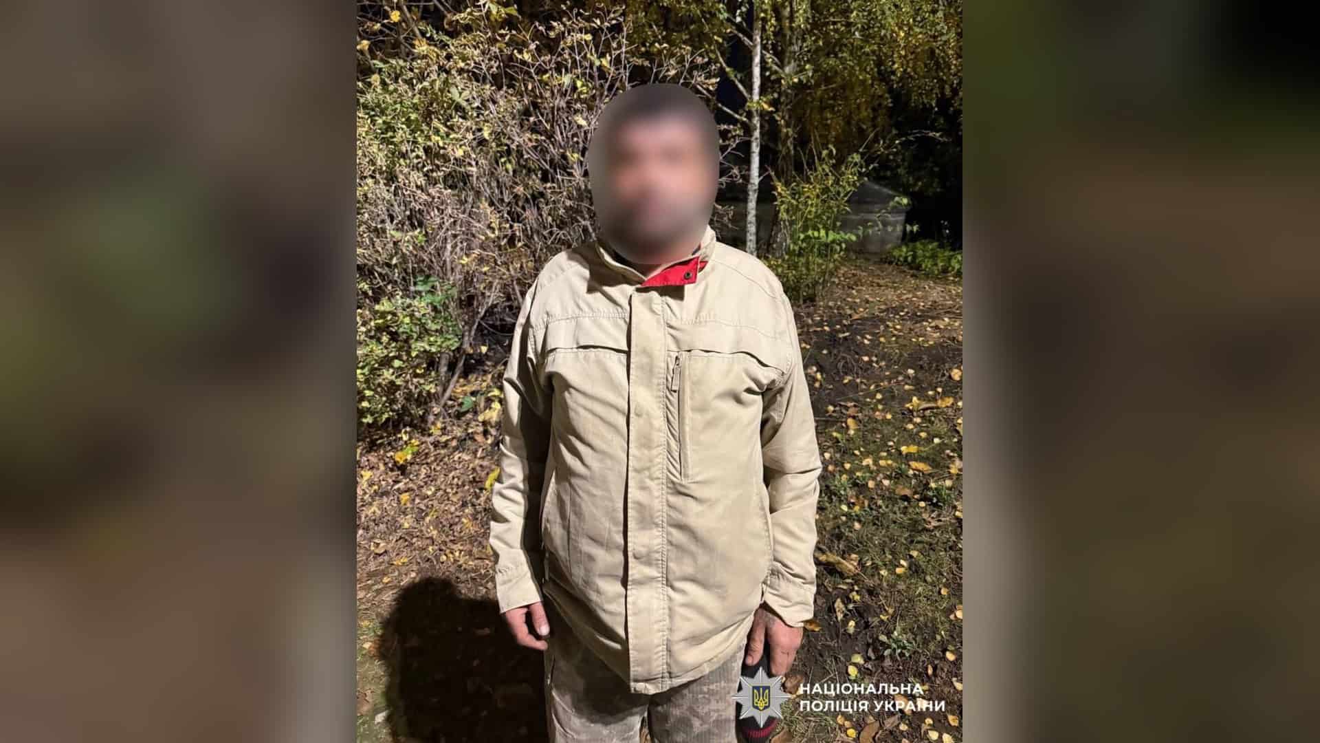 Чоловік у світлій куртці та військових штанях стоїть увечері на вулиці, обличчя на фото розмите