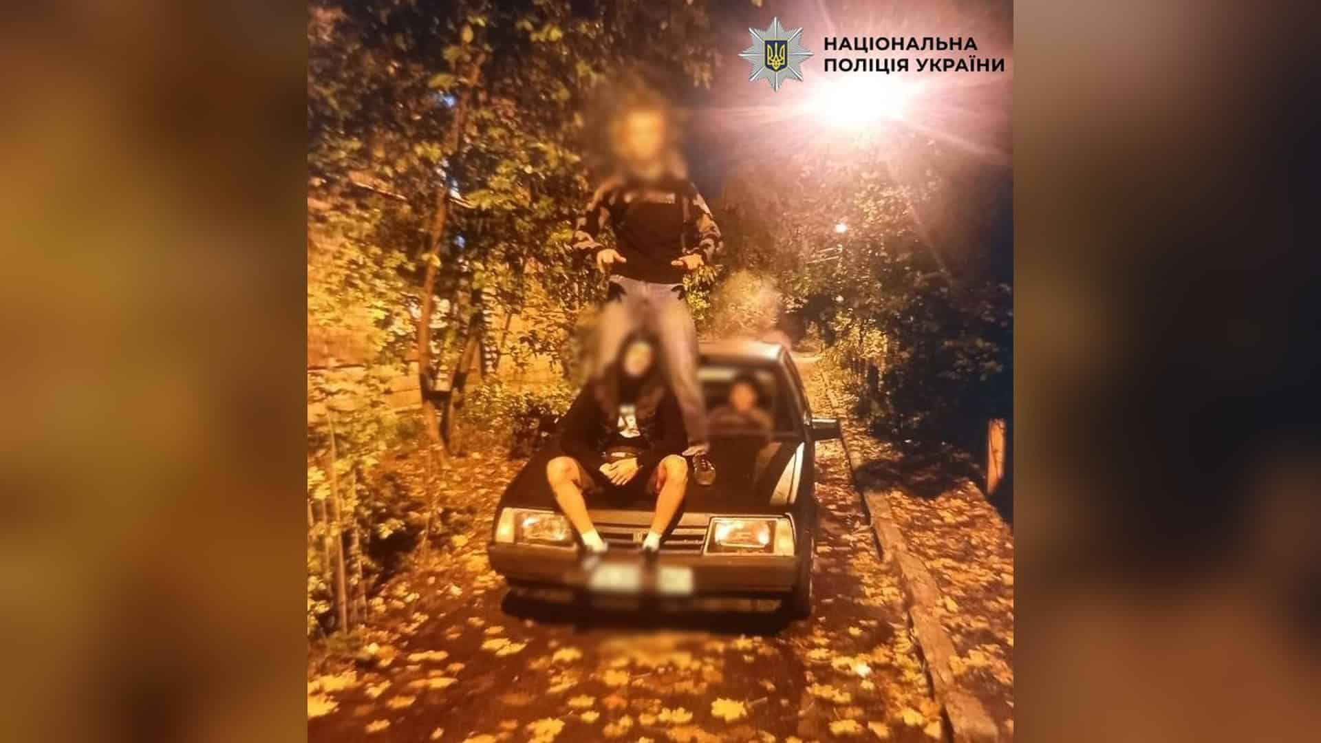 Пасажирів потягу Дніпро-Київ евакуювали через «загрозу мінування» Підлітки позують на капоті та над автомобілем ВАЗ уночі на засипаній листям вулиці, обличчя розмито, логотип Національної поліції України