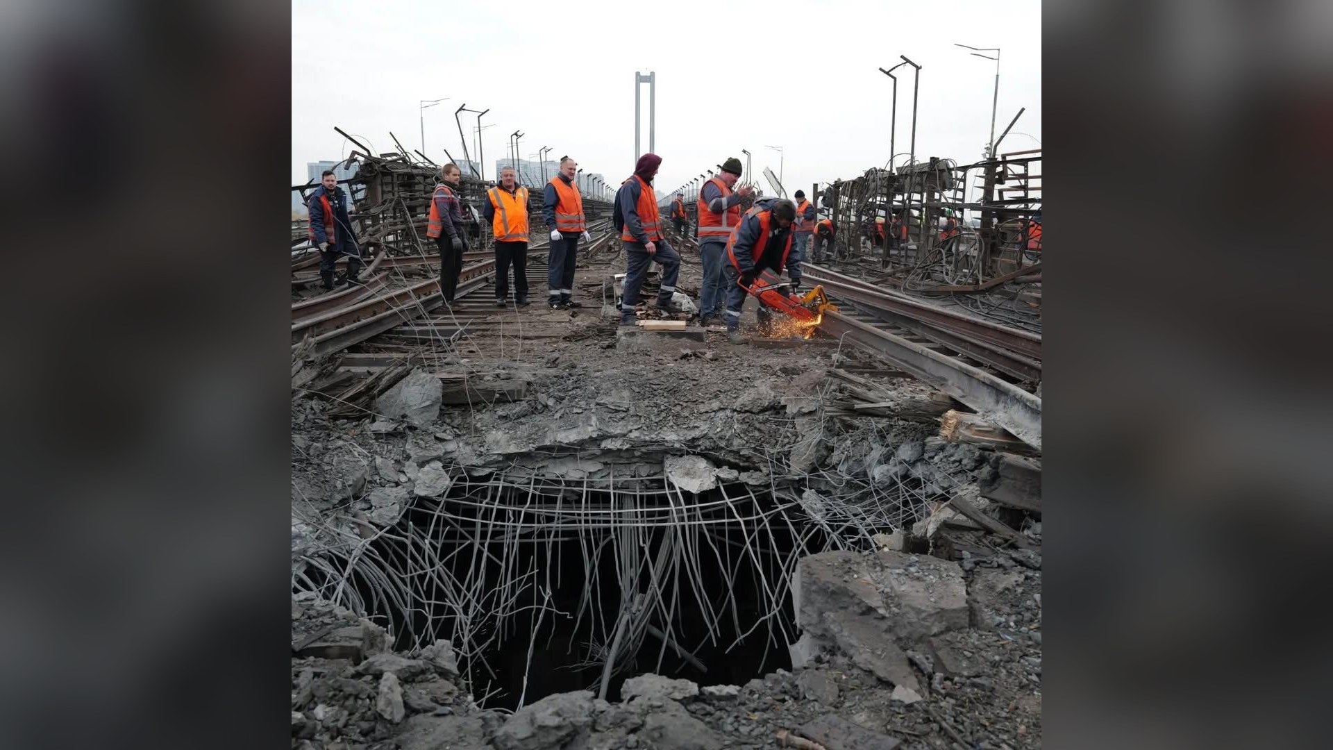 Пробоїна з оголеною арматурою в полотні Південного мосту біля колій метро, поруч працюють ремонтники, Київ, 27 жовтня