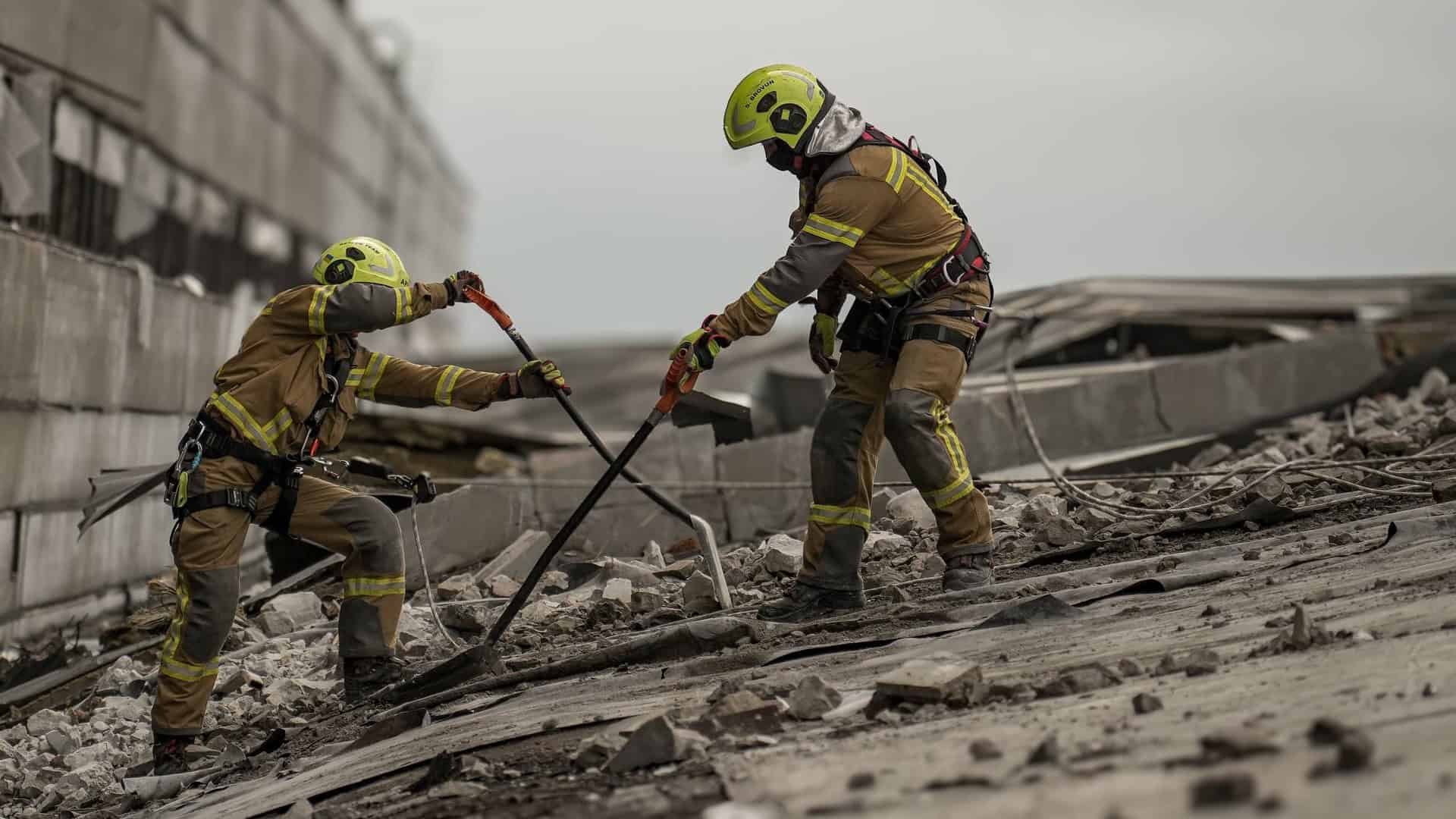 Двоє рятувальників-верхолазів ДСНС Київщини у шоломах і страхувальних поясах розчищають уламки на пошкодженій покрівлі