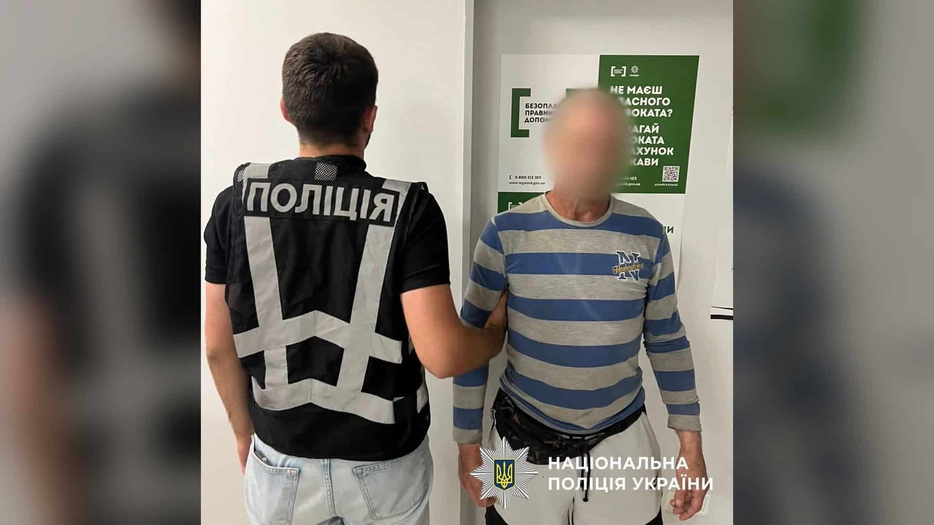 Поліцейський тримає за руку одного з чоловіків, затриманих за розбійний напад на киянку на Столичному шосе