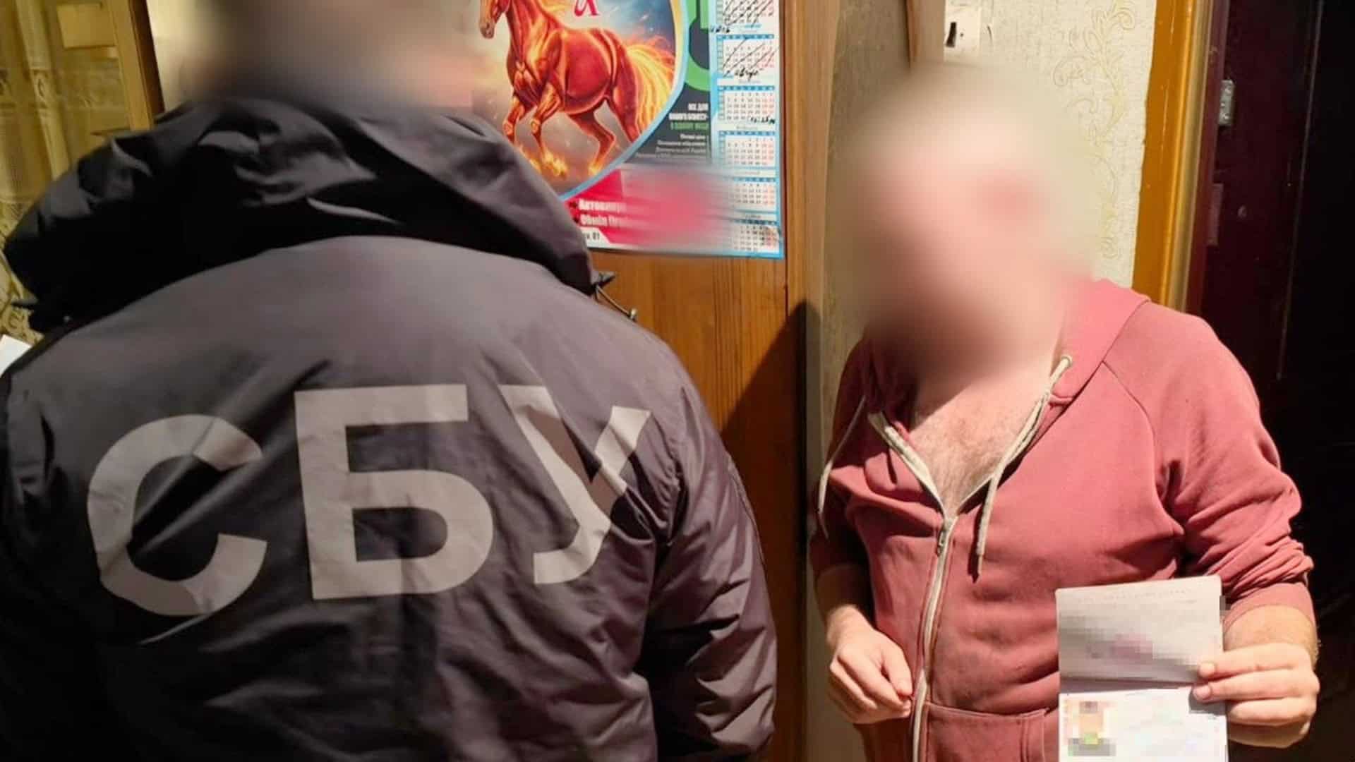 Співробітник СБУ у куртці з написом «СБУ» поруч із чоловіком із розмитим обличчям, який тримає паспорт, під час слідчих дій