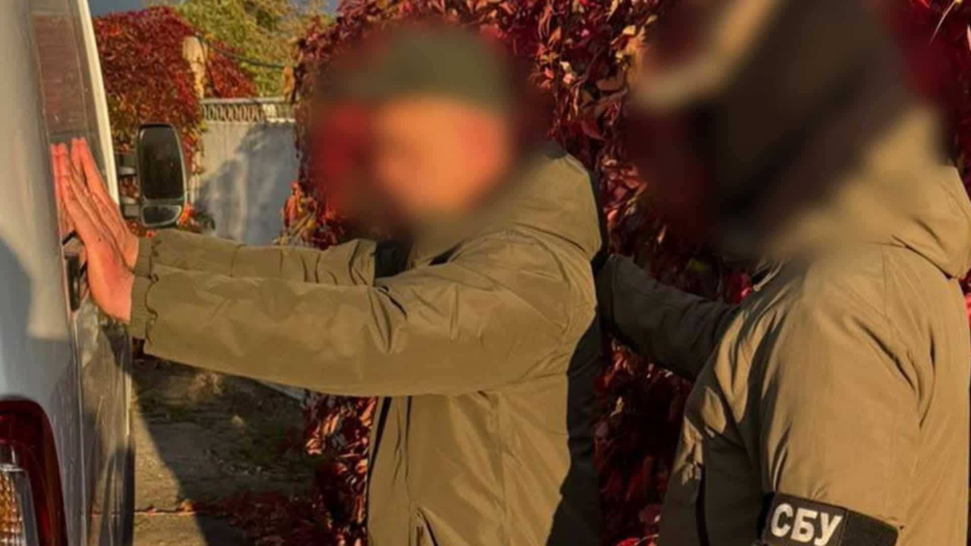 Співробітник СБУ затримує чоловіка біля мікроавтобуса під час викриття схем ухилення від мобілізації, обличчя розмиті
