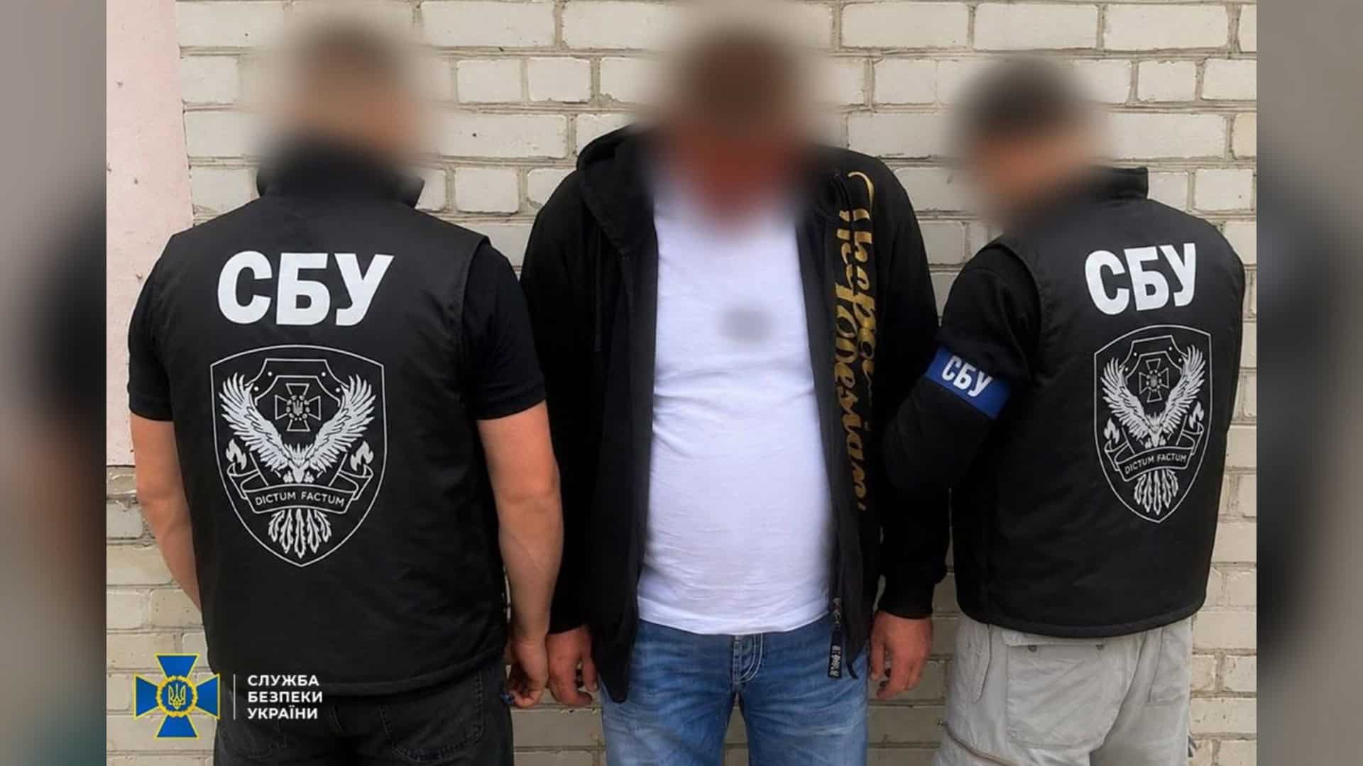 Падіння БпЛА біля АЗС у Голосіївському р-ні: одна людина загинула Двоє співробітників СБУ у чорних жилетах біля затриманого чоловіка в білій футболці на тлі цегляної стіни