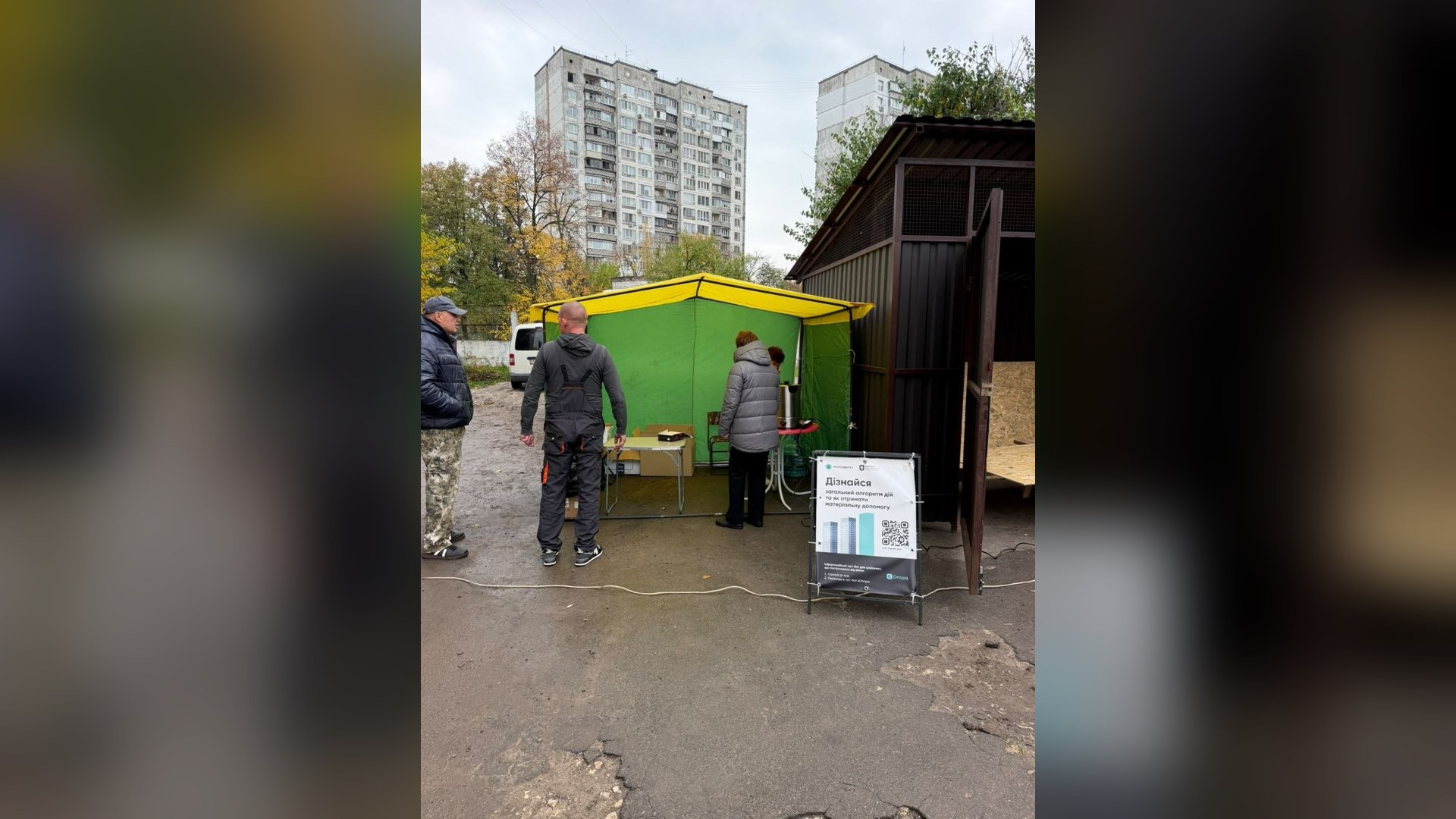 Намет штабу допомоги постраждалим на вулиці Мілютенка в Деснянському р-ні Києва, біля нього люди й стенд з інформацією