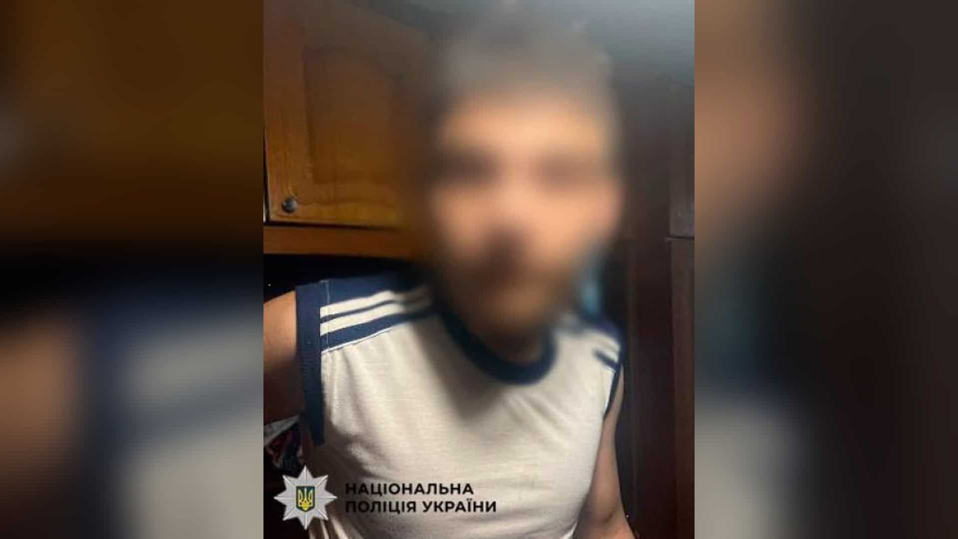 Молодик із розмитим обличчям у білій майці з темними смугами після затримання за пограбування знайомого в Києві