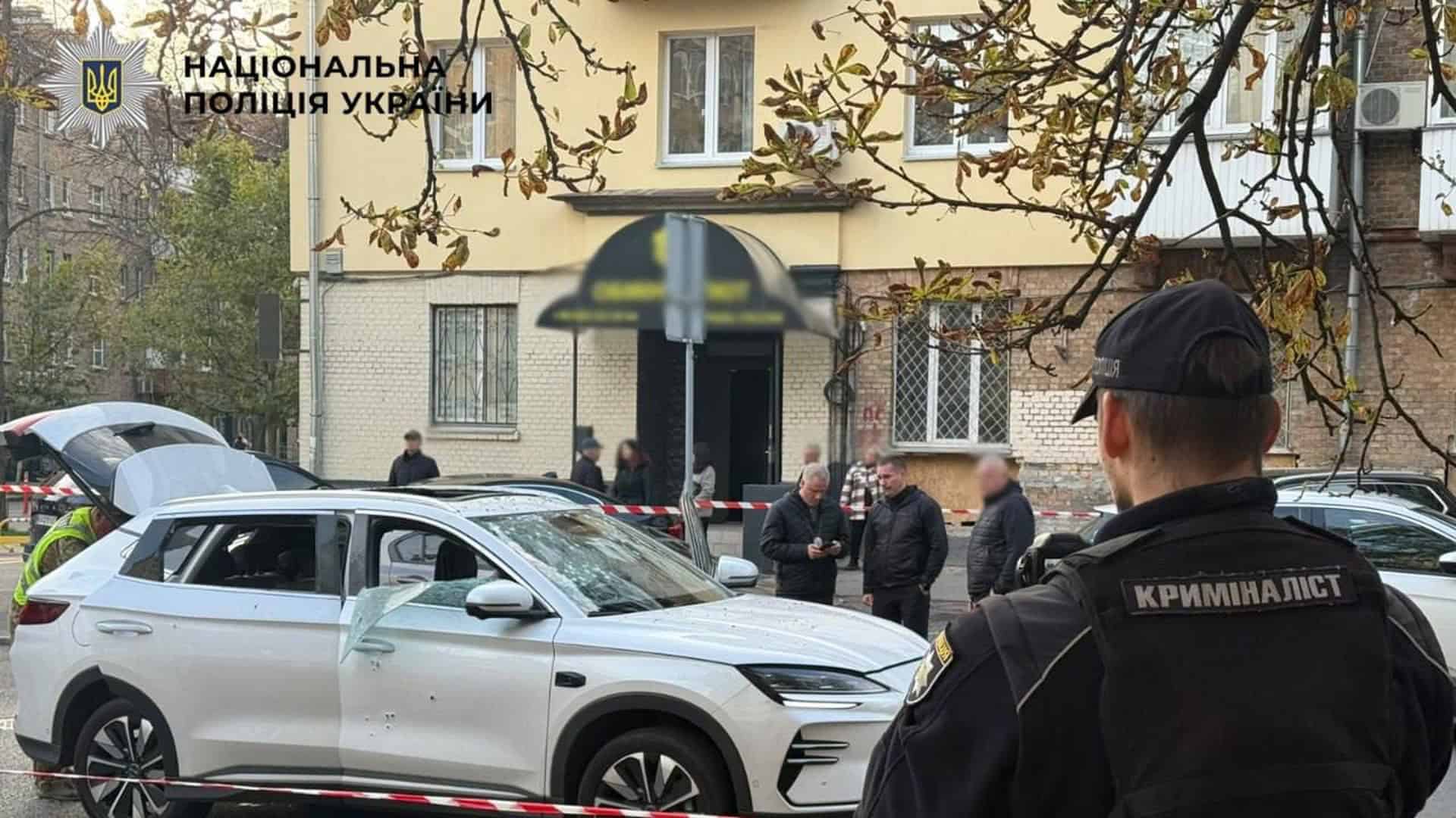 Криміналіст поліції біля пошкодженого білого електромобіля з вибитим склом за огороджувальною стрічкою в Печерському р-ні Києва