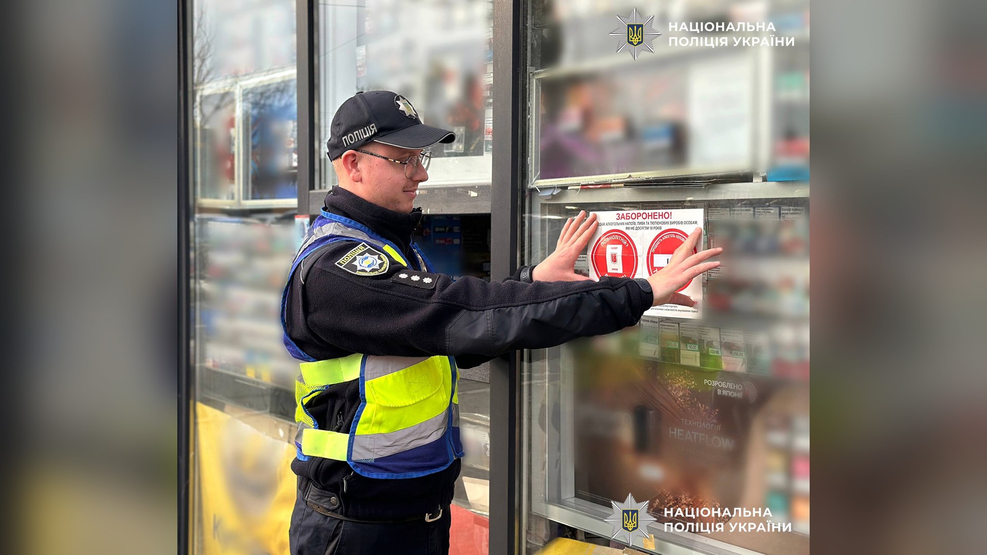 Ювенальний поліцейський клеїть на вітрину кіоску в Києві наліпку про заборону продажу алкоголю й тютюну неповнолітнім