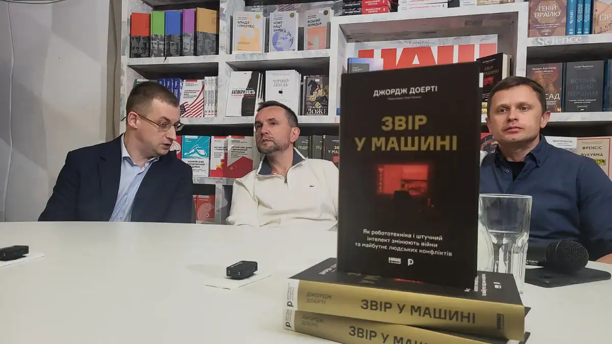 Презентація книги Джорджа Доерті «Звір у машині» в Києві: троє учасників за столом у книгарні, на передньому плані — книга