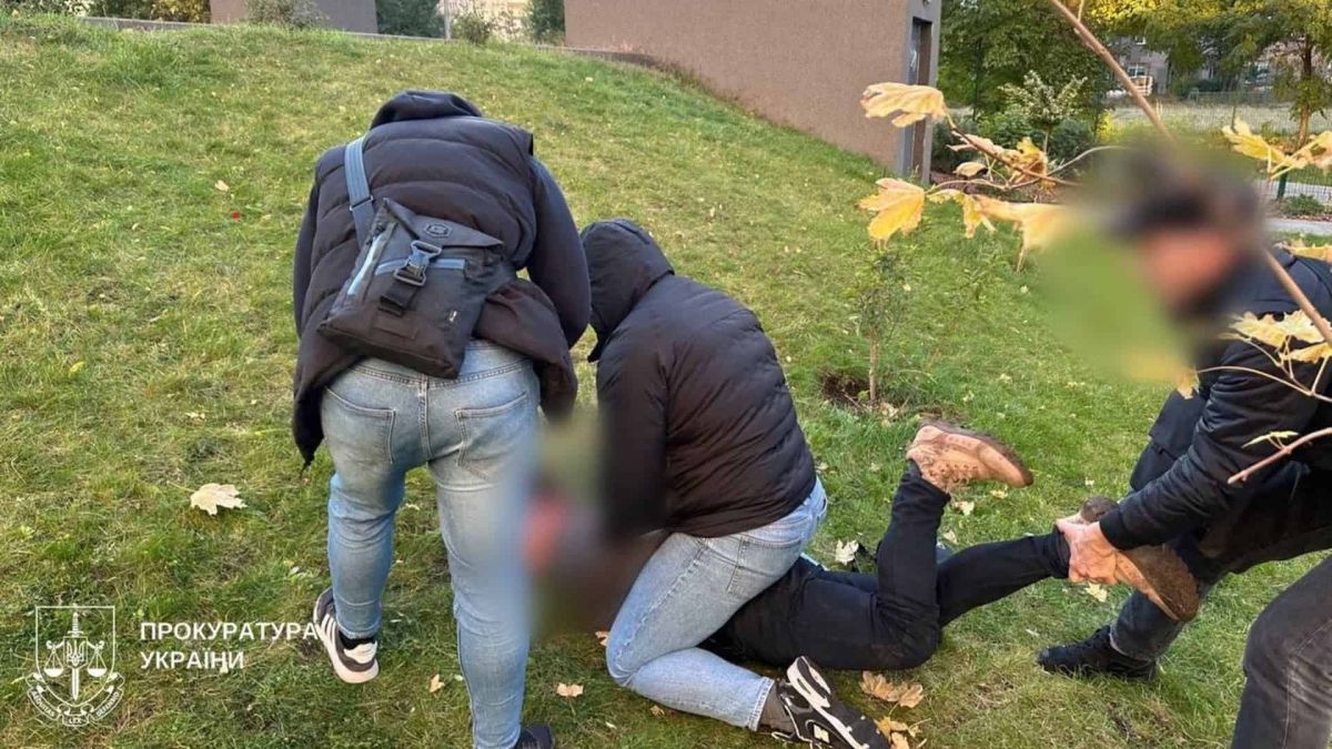 Кілька чоловіків у цивільному затримують людину на траві біля будівлі