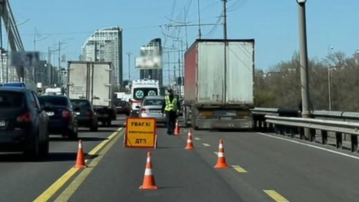 Місце ДТП на проспекті Романа Шухевича в Києві: дорожні конуси, попереджувальний знак та патрульний поліцейський регулює рух