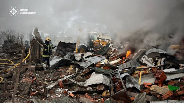 Рятувальник ДСНС Київщини та екскаватор JCB розбирають завали зруйнованої будівлі серед густого диму після ворожої атаки на Київщину