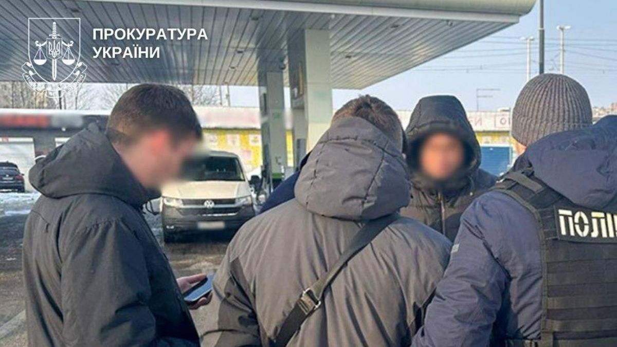 Поліцейські затримують підозрюваного у шахрайстві щодо військовозобов'язаного на тлі заправки в Києві. Чоловік стоїть у наручниках.