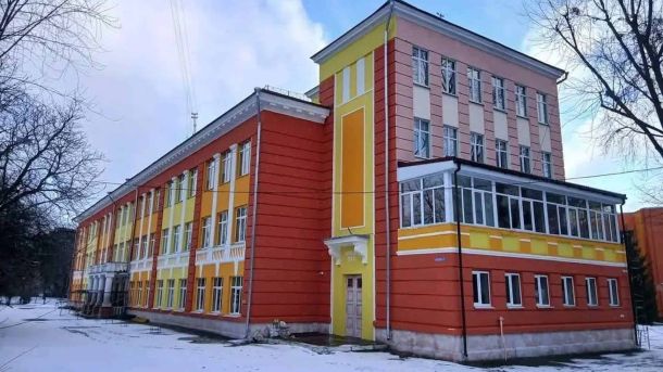 Двоповерхова будівля ліцею №8 на Оболоні у Києві після перефарбування — яскравий вогняно-помаранчевий та жовтий фасад на тлі зимового неба