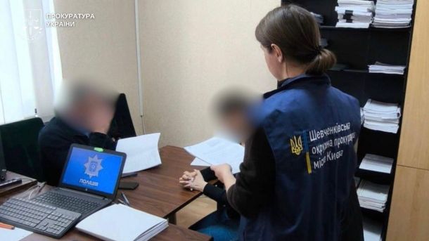 Працівниця Шевченківської окружної прокуратури Києва у жилеті з написом вивчає документи за столом разом із поліцейським під час слідчих дій