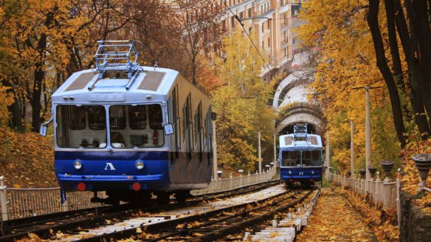 Два синьо-білих вагони київського фунікулера розʼїжджаються на колії серед осіннього листя на Володимирській гірці
