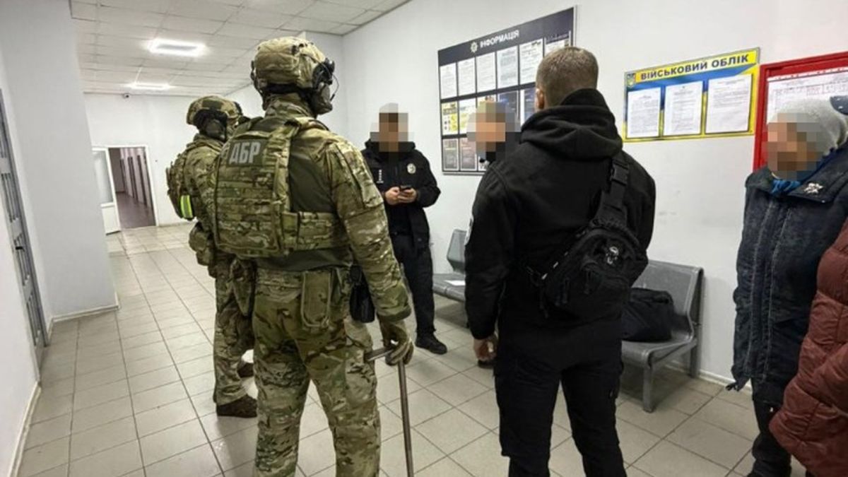 Працівники ДБР стоять з працівниками поліції в приміщенні, схожому на поліцейський відділок, двоє чоловіків у повному бойовому екіпіруванні