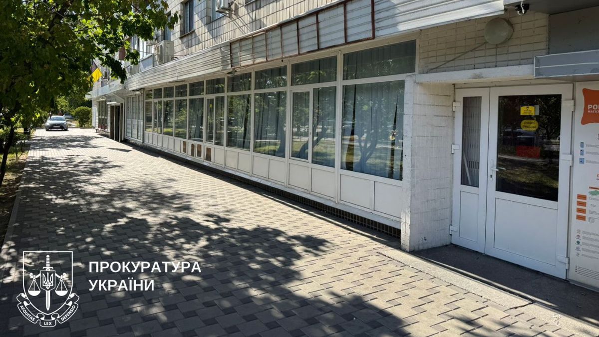 Фасад будівлі з великими вікнами та білими рамами, поруч із тротуаром, викладеним бруківкою