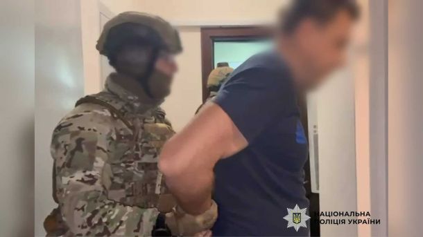 Спецпризначенець у камуфляжі й шоломі веде затриманого чоловіка з розмитим обличчям у приміщенні