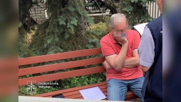 Головні новини Києва | Kyiv.News Чоловік у червоній футболці сидить на лавці поруч із правоохоронцем під час затримання адвоката в Києві, фото прокуратури