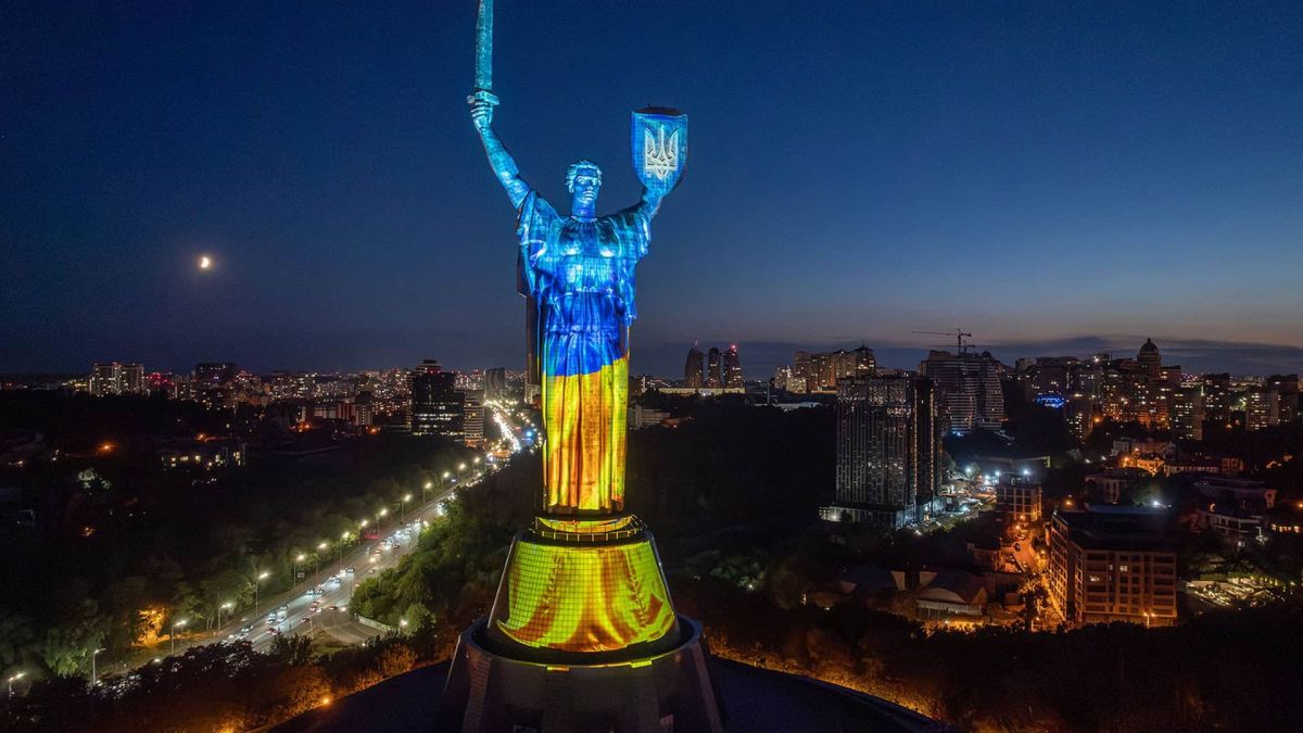 Підсвічений синьо-жовтими кольорами монумент «Батьківщина-Мати» вночі на тлі нічного Києва та автомагістралі