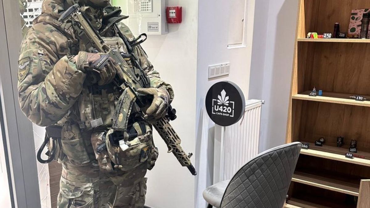Озброєний поліцейський у камуфляжі проводить обшук у магазині мережі U420 з вивіскою cafe-shop на стіні