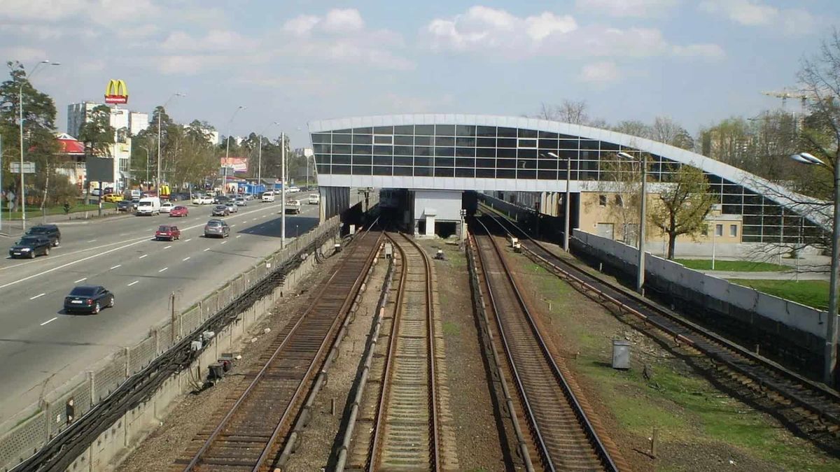 Наземна станція червоної лінії Київського метро: колії перед станцією та проспект з автомобілями поруч