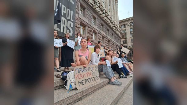 Учасники акції протесту з плакатами проти підвищення тарифів на проїзд сидять на сходах під будівлею КМДА