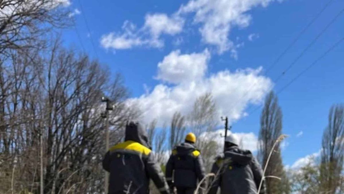 Три енергетики ДТЕК у спецодязі йдуть вздовж лінії електропередачі серед дерев під час ліквідації аварій після негоди на Київщині у квітні 2026 року