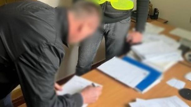 Чоловік із заблюреним обличчям підписує документи, які лежать на столі в поліції. Поряд з чоловіком стоїть працівник поліції