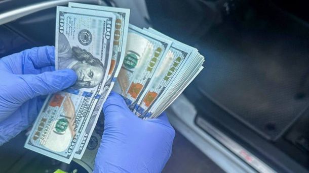 Рука в синій рукавичці тримає пачку стодоларових купюр в автомобілі під час затримання поліцією