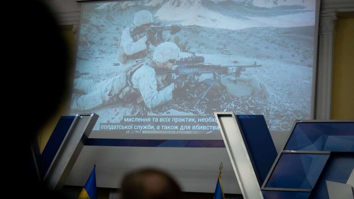 Глядачі дивляться кінопоказ на великому екрані: кадр із солдатами з субтитрами, поруч прапори України