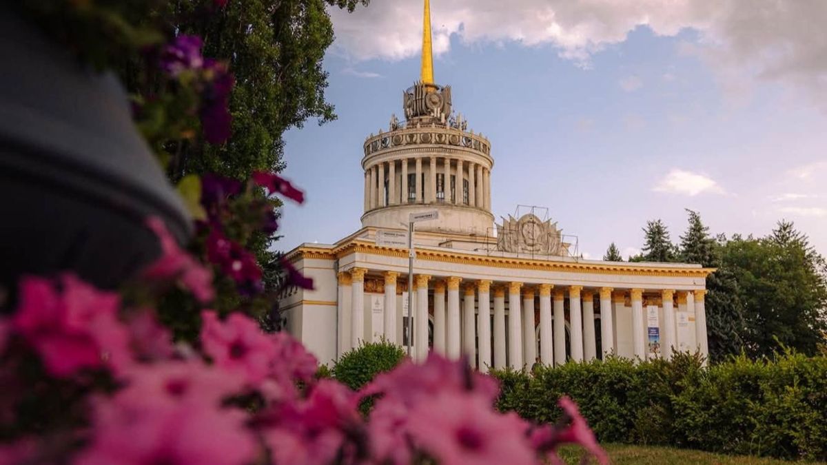 Головний павільйон ВДНГ зі шпилем на тлі неба, у розмитому передньому плані рожеві квіти петунії